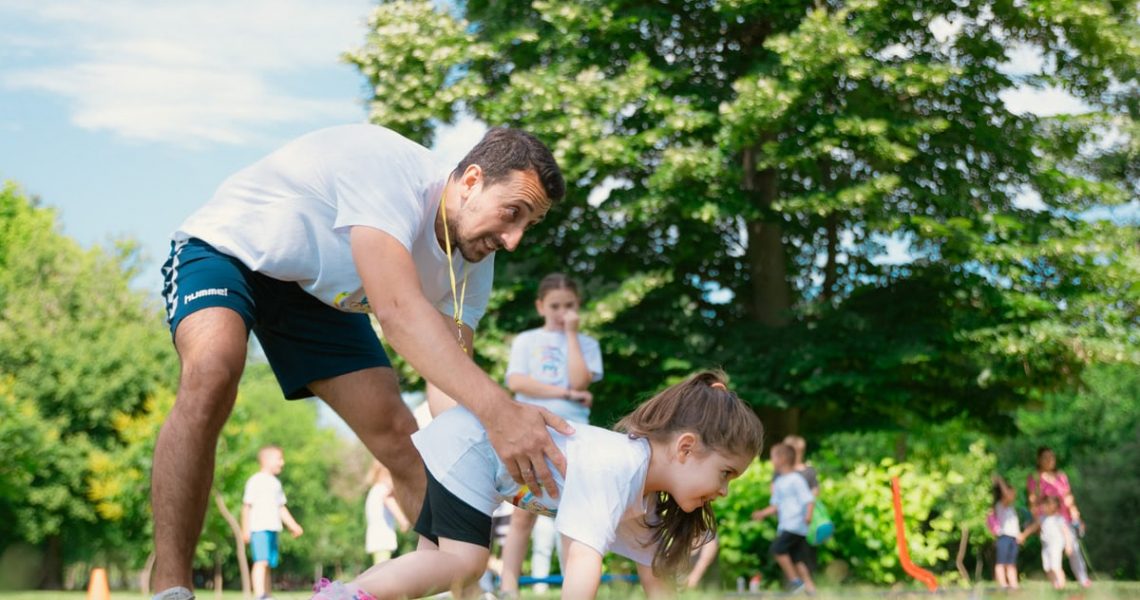 Children exercising with instructor outdoors, enjoying physical education in summer park setting.